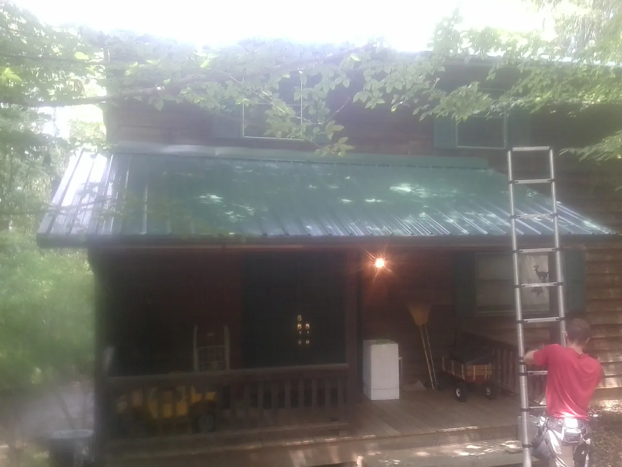 Worker on a ladder at the green porch roof of a wooded cabin in Ogden